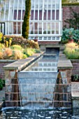 BROUGHTON GRANGE, OXFORDSHIRE: DESIGNER TOM STUART-SMITH - POOL AND WATERFALL IN THE WALLED GARDEN WITH GREENHOUSE BEHIND - SPRING, WATER, STEPPING STONES, RILL, CANAL