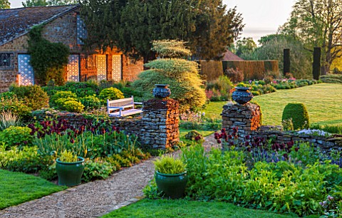 PETTIFERS_OXFORDSHIRE_PATH_DOWN_TO_LAWN_WITH_PEDESTALS_WITH_LEAD_URNS_TULIP_BLACK_PARROT_CORNUS_ALTE