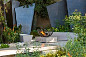 CHELSEA FLOWER SHOW 2016: TELEGRAPH GAREDEN DESIGNED BY ANDY STURGEON - LIMESTONE BRIDGE AND BRONZE FINS BESIDE WATER. LIMESTONE SEATS AND FIREPIT - SEATING, BENCH, BENCHES, FIRE