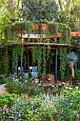 CHELSEA FLOWER SHOW 2016: THE WINTON BEAUTY OF MATHEMATICS GARDEN - DESIGNER NICK BAILEY: COPPER BAND ABOVE BELVEDERE - PATIO WITH HANGING PLANTS.