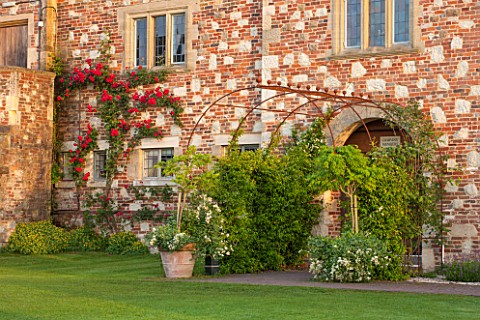 GLYNDEBOURNE_EAST_SUSSEX__RED_ROSE_GROWING_AGAINST_WALL_AND_METAL_ARCHWAY__FORMAL_ROSES_ENGLISH_SUMM