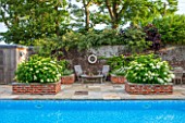 THE COACH HOUSE, SURRY:WALLED SWIMMING POOL AREA WITH RAISED BRICK BEDS CONTAINING HYDRANGEA ARBORESCENS ANNABELLE. SUMMER, A PLACE TO SIT,TABLE & CHAIRS,ENTERTAIN,LEISURE,GARDEN