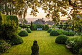 GREYHOUNDS, BURFORD, OXFORDSHIRE:THE MAIN BORDERS AND LAWN IN DAWN LIGHT.FRAMED BY YEW TOPIARY, HORNBEAM AND CLIPPED BOX. WITH WOODEN BENCH. A PLACE TO SIT, SUMMER, GARDEN, CLASSIC