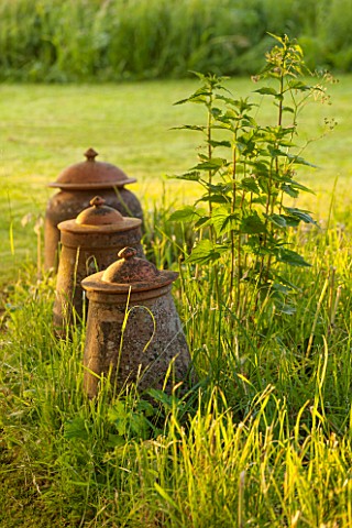GREYHOUNDS_BURFORD_OXFORDSHIRE_OLD_LIDDED_TERRACOTTA_JARSURNS_IN_MEADOW_INFORMAL_STYLE