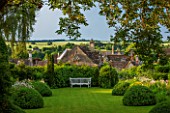 GREYHOUNDS, BURFORD, OXFORDSHIRE: COTTAGE STYLE LAWN AND BORDER WITH WOODEN BENCH. BOX DOMES, YEW TOPIARY, SUNLIGHT. CLASSIC COUNTRY GARDEN, SUMMER.