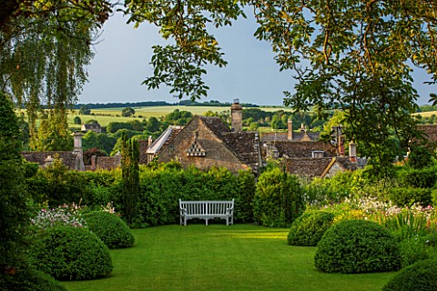 GREYHOUNDS_BURFORD_OXFORDSHIRE_COTTAGE_STYLE_LAWN_AND_BORDER_WITH_WOODEN_BENCH_BOX_DOMES_YEW_TOPIARY