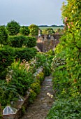 GREYHOUNDS, BURFORD, OXFORDSHIRE: VIEW TO PATH WITH COTTAGE STYLE BORDERS AND ANTIQUE WINTER CLOCHES. WITH YEW TOPIARY. CLASSIC COUNTRY GARDEN. INFORMAL, SUMMER