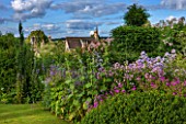 GREYHOUNDS, BURFORD, OXFORDSHIRE:COUNTRY GARDEN & COTTAGE BORDER WITH VALERIANA OFFICINALIS, CAMPANULA VARS, HOLLYHOCKS & ERYNGIUM BOURGATII. YEW TOPIARY. SUMMER, LILAC,PURPLE