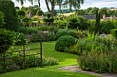 GREYHOUNDS, BURFORD, OXFORDSHIRE: COUNTRY COTTAGE GARDEN SCENE WITH LAWN AND HERBACEOUS BORDERS. WITH VIEWS ACROSS THE ROOFS OF BURFORD. PERENNIAL, SUMMER, INFORMAL.