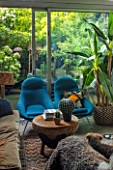 ABIGAIL AHERN HOUSE, LONDON: THE LIVING ROOM AND VIEW ONTO PATIO - BLUE CHAIRS, INSIDE OUT. CUSHIONS, SITTING ROOM, DARK, INTERIOR, NILE OTTOMAN STOOL, FAKE GOLDENBALL CACTUS