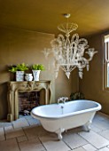 ABIGAIL AHERN HOUSE, LONDON: BATHROOM PAINTED WITH WOOSTER OLIVE PAINT, BATH, FIREPLACE, FAUX PLANTS, NEO - BAROQUE CHANDELIER