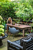 ABIGAIL AHERN HOUSE, LONDON: ABIGAIL IN HER GARDEN, PATIO WITH TABLE, CHAIRS, FAUX STAGHORN PLANT IN CONTAINER, OUTDOOR KITCHEN