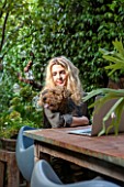 ABIGAIL AHERN HOUSE, LONDON: ABIGAIL IN HER GARDEN WITH PET DOG MAUD, PATIO WITH TABLE, CHAIRS, FAUX STAGHORN PLANT IN CONTAINER