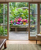 HENRIETTA COURTAULDS HOUSE, NOTTING HILL, LONDON: THE LAND GARDENERS - VIEW THROUGH DOORS TO SMALL TOWN GARDEN. PATIO, TERRACE, STEPS, TABLE WITH CUT DAHLIA FLOWERS. GREEN