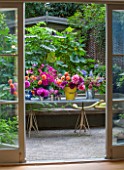 HENRIETTA COURTAULDS HOUSE, NOTTING HILL, LONDON: THE LAND GARDENERS - VIEW THROUGH DOORS TO SMALL TOWN GARDEN. PATIO, TERRACE, STEPS, TABLE WITH CUT DAHLIA FLOWERS. GREEN
