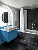 MORTON HALL, WORCESTERSHIRE: BATHROOM WITH ARCHED WINDOW, FREE STANDING CIRCULAR MIRROR WITH BLUE PAINTED CABINETS AND OVAL SHOWER CURTAIN RAIL. BLACK MARBLE TILES