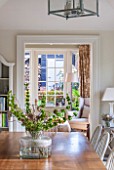 THE COACH HOUSE,SURREY: VIEW INTO GARDEN ROOM FROM BREAKFAST ROOM WITH TABLE AND CHAIRS WITH VASE OF FRESH FLOWERS/FOLIAGE