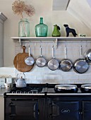 THE COACH HOUSE,SURREY: THE KITCHEN WITH DETAIL OF SHELF WITH HANGING POTS AND PANS ABOVE BLACK AGA. DECORATIVE, COUNTRY KITCHEN.