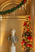 VAUX LE VICOMTE, FRANCE: THE ENTRANCE HALL DECORATED FOR CHRISTMAS. A BUST SITS BESIDE SEASONAL SWAGS AND DECORATIONS