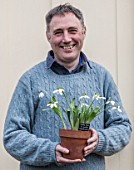 HILL CLOSE GARDENS, WARWICK: HEAD GARDENER GARY LEAVER HOLDING SNOWDROPS IN TERRACOTTA CONTAINER - GALANTHUS, MAN