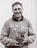 HILL CLOSE GARDENS, WARWICK: BLACK AND WHITE IMAGE OF HEAD GARDENER GARY LEAVER HOLDING SNOWDROPS IN TERRACOTTA CONTAINER - GALANTHUS, MAN