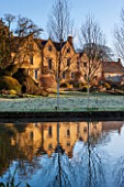 ABLINGTON MANOR, GLOUCESTERSHIRE: FEBRUARY VIEW TO THE HOUSE AT SUNRISE WITH RIVER COLNE , LAWN AND TOPIARY. FORMAL, ENGLISH, GARDEN, EARLY SPRING. REFLECTION, REFLECTIONS