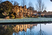 ABLINGTON MANOR, GLOUCESTERSHIRE: FEBRUARY VIEW TO THE HOUSE AT SUNRISE WITH RIVER COLNE , LAWN AND TOPIARY. FORMAL, ENGLISH, GARDEN, EARLY SPRING. REFLECTION, REFLECTIONS