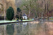 ABLINGTON MANOR, GLOUCESTERSHIRE: VIEW ACROSS COLN RIVER TO WOODEN FOOT BRIDGE. SUNRISE, CLASSIC, COUNTRY GARDEN, COTSWOLDS, ROMANTIC, ROMANCE, WINTER, EARLY SPRING, SUMMERHOUSE