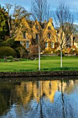 ABLINGTON MANOR, GLOUCESTERSHIRE: VIEW ACROSS RIVER COLN TO MANOR HOUSE. MARCH, EARLY SPRING, LATE WINTER, WATER, RIVER, COUNTRY, GARDEN, ENGLISH, TOPIARY