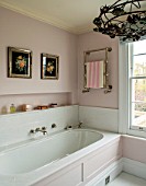 LONDON HOUSE DESIGNED BY JULIE SIMONSEN. PINK BATHROOM. PALE PINK PANELLED BATH WITH TOWEL RAIL AND ANTIQUE FLOWER PRINTS DISPLAYED ON WALL