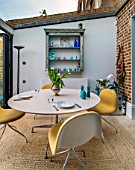 LONDON HOUSE DESIGNED BY JULIE SIMONSEN. MORNING ROOM WITH EXPOSED BRICKWORK AND CIRCULAR TABLE WITH CONTEMPORARY YELLOW CHAIRS. LEADING OUT TO GARDEN.