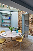 LONDON HOUSE DESIGNED BY JULIE SIMONSEN. MORNING ROOM WITH EXPOSED BRICKWORK AND CIRCULAR TABLE WITH YELLOW CONTEMPORARY CHAIRS