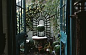 VIEW THROUGH BACK DOOR/FRENCH WINDOWS ONTO BRICK TERRACE OF SMALL TOWN GARDEN WITH ARCHED TRELLIS & HEDERA ON WALL & BOX TREE IN CONTAINER DUSTED WITH SNOW. DESIGNER: ANTHONY NOEL