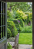 BUTTER WAKEFIELD HOUSE, LONDON: VIEW OUT OF KITCHEN DOORWAY TO GARDEN WITH CLIPPED TOPIARY BOX PYRAMIDS AND LAWN. WOODEN BENCH, CHAIRS, DOOR, SUMMER