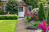 COTTAGE ROW, DORSET: BRICK PATH AND BORDER, SPRING, ALLIUMS, GLADIOLUS COMMUNIS SUBSP. BYZANTINUS, WALL, HOUSE, MORNING, DOOR, LAWN
