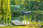 THE OLD RECTORY, QUINTON, NORTHAMPTONSHIRE: DESIGNER ANOUSHKA FEILER: NATURAL SWIMMING POND, DECK, WHITE WOODEN SCULPTURE, SUNLOUNGERS. WATER, LAKE, POOL, DECKING