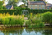 THE OLD RECTORY, QUINTON, NORTHAMPTONSHIRE: DESIGNER ANOUSHKA FEILER: NATURAL SWIMMING POND, HOUSE, WILDFLOWER MEADOW, ARCH THROUGH CARPINUS BETULUS HEDGE. HEDGING, HEDGES