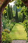 WOLLERTON OLD HALL, SHROPSHIRE: YEW WALK: ARCH IN WALL, GATE, GRASS, PATH, PYRAMID, TOPIARY CLIPPED YEW. FORMAL, ARTS AND CRAFTS, GREEN, LAWN, MAY, SUMMER