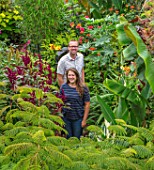 SWEETBRIAR, KENT: STEVE EDNEY, LOUISE DOWLE IN GARDEN WITH BIG LEAVES AND FOLIAGE OF PLANTS. GREEN, PEOPLE, GARDEN, SUMMER, ALBIZIA JULIBRISSIN ROSEA, MUSA SIKKIMENSIS, AMARANTHUS