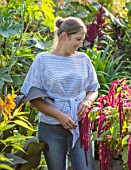 SWEETBRIAR, KENT: LOUISE DOWLE IN THE GARDEN SURROUNDED BY BIG LEAVES AND FOLIAGE OF PLANTS. GREEN, PEOPLE, GARDEN, SUMMER. RICINUS COMMUNIS BLUE GIANT. AMARANTHUS VELVET CURTAINS