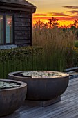 PRIVATE GARDEN, SURREY: DESIGNER ANTHONY PAUL: DECKED GARDEN, CONTAINERS, WATERLILIES. DECKING, ROUND, CIRCULAR, SUNSET, EVENING, LIGHT, FORMAL, SMALL, ENGLISH, COUNTRY