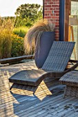 PRIVATE GARDEN, SURREY: DESIGNER ANTHONY PAUL: DECKED GARDEN, CONTAINER WITH STIPA, DECKING, DECKCHAIR, DECK CHAIR, EVENING, LIGHT, FORMAL, SMALL, ENGLISH, COUNTRY