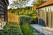 PRIVATE GARDEN, SURREY: DESIGNER ANTHONY PAUL: DECKED GARDEN, DECKING, POND, WATER, EQUISETUM HYEMALE, HORSETAIL, BUILDINGS, CALAMAGROSTIS, FORMAL, SMALL, ENGLISH, COUNTRY