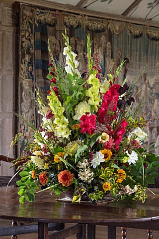 PARHAM_SUSSEX_THE_LONG_GALLERY__CONTAINER_FLOWER_DISPLAY_WITH_GLADIOLUS_DAHLIAS_ZINNIAS_FOLAIGE_OF_B