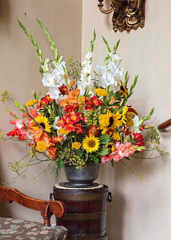 PARHAM_SUSSEX_ENTRANCE_HALL__CONTAINER_WITH_SUNFLOWERS_RED_ALSTROEMERIA_GLADIOLUS_AND_BRONZE_FENNEL