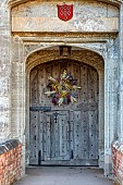 BADDESLEY CLINTON, WARWICKSHIRE: THE NATIONAL TRUST- CHRISTMAS, 15TH AND 16TH CENTURY MOATED MANOR HOUSE. GATEHOUSE WOODEN DOOR, HOME GROWN, HOMEMADE DRIED FLOWER WREATH
