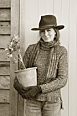 HERTFORDSHIRE HELLEBORES, LORNA JONES: BLACK AND WHITE IMAGE OF LORNA JONES HOLDING A TERRACOTTA CONTAINER OF HELLEBORES