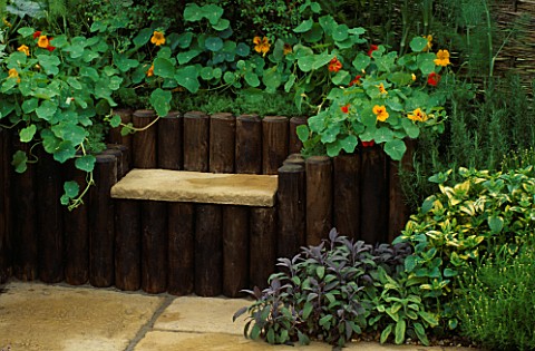 STONE_SEAT_SUNK_INTO_WOODEN_LOGS_SURROUNDED_BY_HERBS_AND_NASTURTIUMS_HOME_FARM_TRUST__CHELSEA_FLOWER