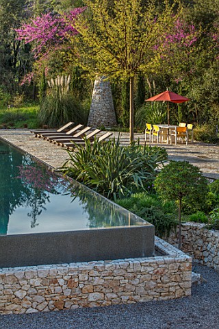 SKOPOS_DESIGN_CORFU_RAISED_BLACK_INFINITY_POOL_WITH_REFLECTIONS_PATIO_AREA_PAVED_SEATING_DINING_CHAI