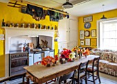 THE OLD PARSONAGE, LITTLE BREDY, DORSET: THE KITCHEN WITH DINING TABLE AND CHAIRS, SOFA, RANGE COOKER. TULIPS PICKED FROM THE GARDEN IN VASES.YELLOW INTERIOR, HOME,COUNTRY STYLE.